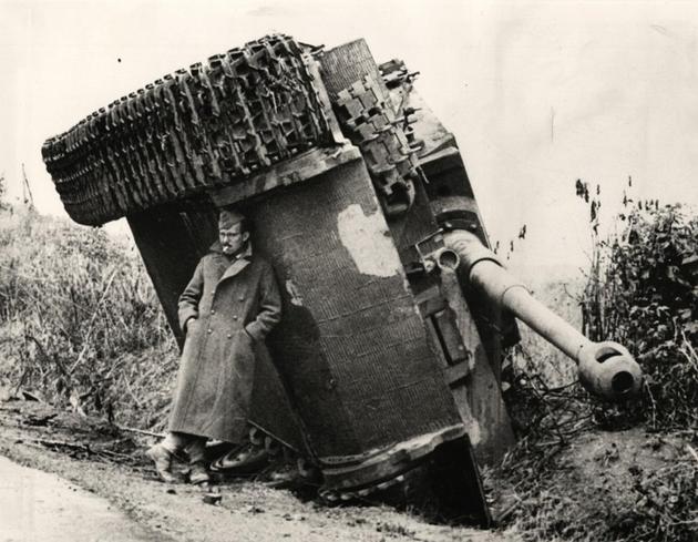 American soldier hiding from rain under a overturned  tiger tank